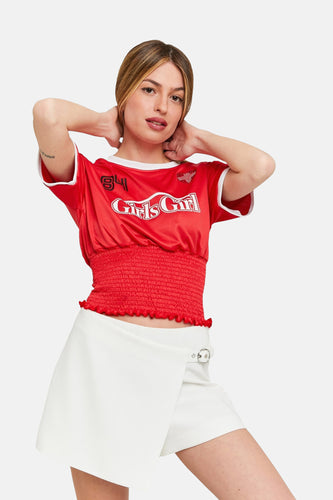 Vrouw met rode top en witte rok, handen in de nek, lichte achtergrond.