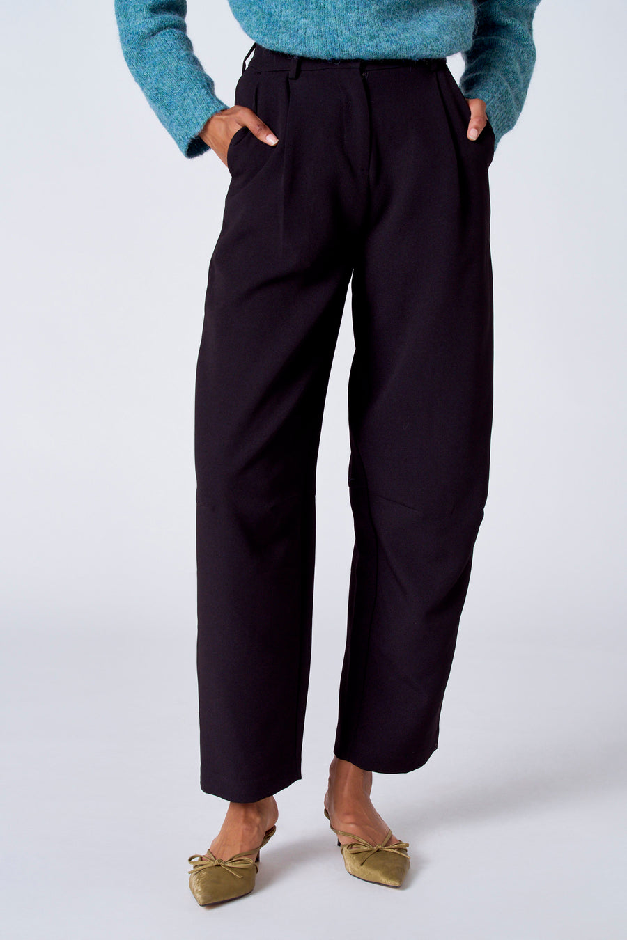 Pantalon de costume noir de SUNSET STUDIO, avec des poches à l'arrière et une main sur le pantalon.