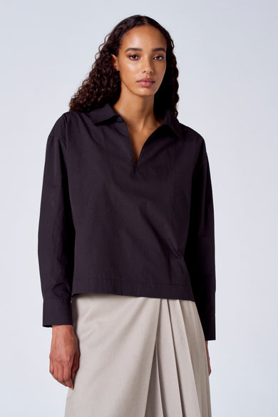 Blouse noire à manches longues de SUNSET STUDIO, portée avec une jupe beige plissée.