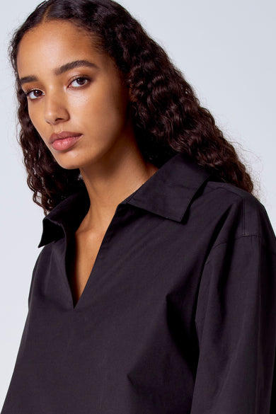 Blouse noire à manches longues de SUNSET STUDIO, avec un col ouvert et une texture lisse.