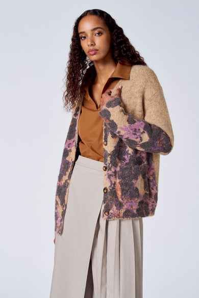 Pull-over marron avec col V de SUNSET STUDIO, porté sous un gilet tricoté à motifs floraux et une jupe beige.