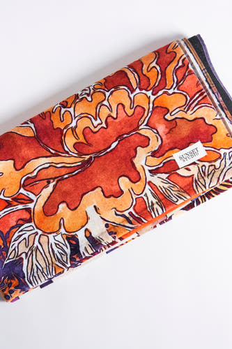 Oranje strandkleding van SUNSET STUDIO, met een opvallend bloemmotief in rood, oranje en paars.