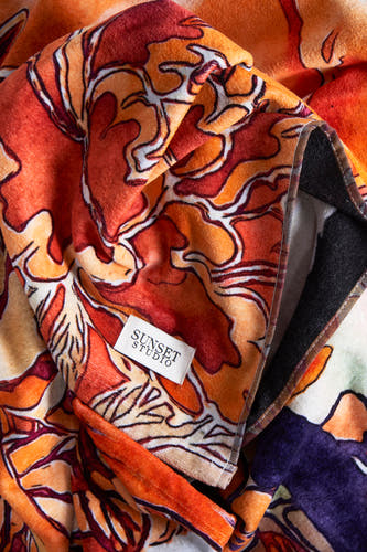 Maillot de bain orange de SUNSET STUDIO, avec un motif floral abstrait en tons rouges et oranges et une bordure noire.