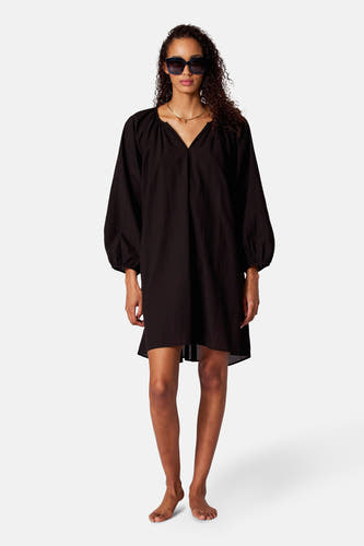 Robe noire avec des manches longues de SUNSET STUDIO, montrée en arrière-plan avec des boucles élégantes.