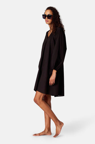 Robe noire avec des manches longues de SUNSET STUDIO, portée avec un chapeau de soleil, en vue de dos.