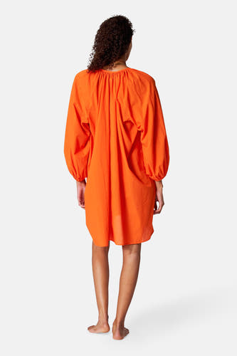 Maillot orange à longues manches de SUNSET STUDIO, vu de dos avec des cheveux bouclés.