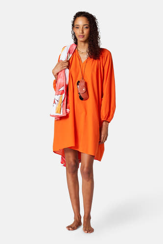 Manteau orange à longues manches de SUNSET STUDIO, avec un foulard sur l'épaule et un accessoire marron autour du cou.