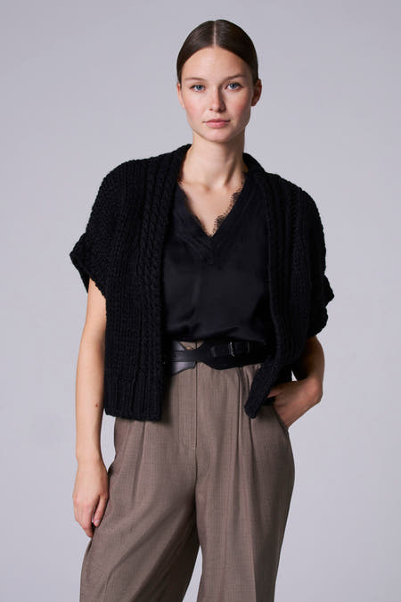 Gilet de denim noir d'Astrid Black Label, avec une texture crochetée et porté sur une blouse noire et un pantalon marron.