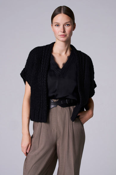 Gilet de denim noir d'Astrid Black Label, avec une texture crochetée et porté sur une blouse noire et un pantalon marron.