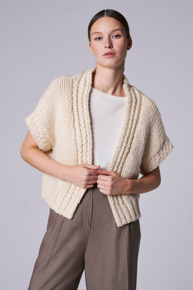 Gilet blanc d'Astrid Black Label, porté sur un shirt blanc et associé à un pantalon marron.