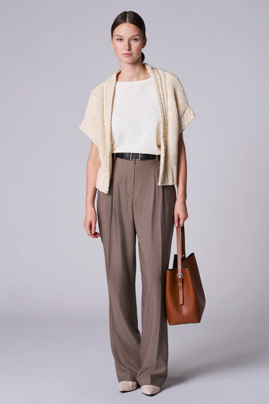 Gilet blanc d'Astrid Black Label, porté sur une chemise crème avec un pantalon marron et une sacoche en cuir.