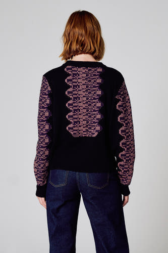Pull-over noir avec col rond de Clouds of Fashion, avec un motif géométrique rose sur le dos et les manches, porté avec des jeans bleus foncés.