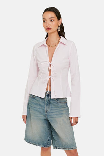Chemise rose à manches longues de TALLY WEIJL, avec fermeture éclair, associée à un short en denim et des bijoux dorés.