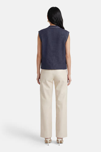 Gilet sans manches bleu d'ADORE, avec surpiqûres blanches, combiné avec un pantalon en cuir de couleur crème et des talons hauts.