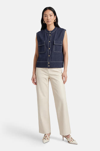 Gilet court sans manches ADORE, avec surpiqûres contrastées, porté avec un pantalon crème et des talons.