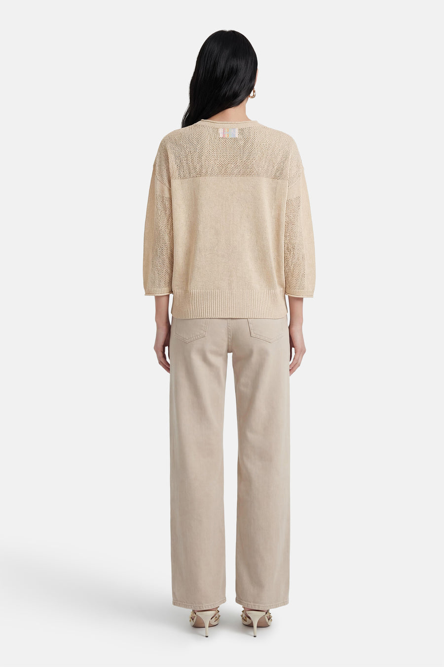 Pull écru ADORE, avec un tricot ajouré et porté avec un pantalon beige et des talons aiguilles.