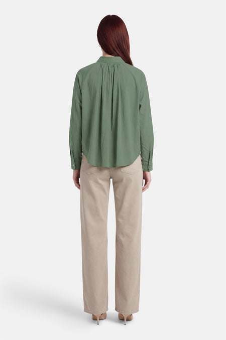 Chemise verte ADORE, à manches longues et avec des plis dans le dos, combinée avec un pantalon beige et des talons.