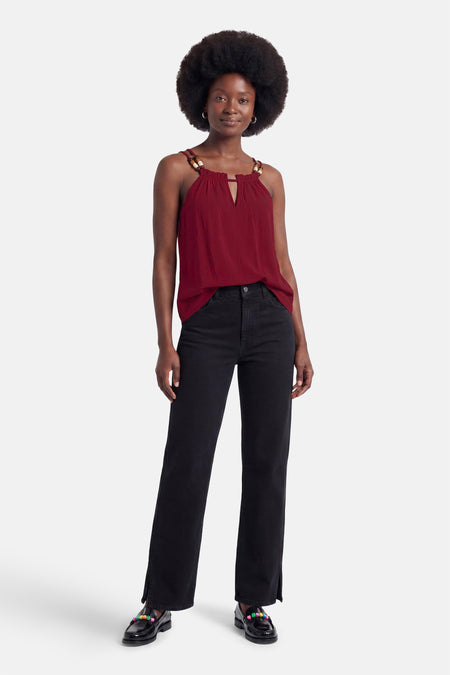 Rode mouwloze blouse met halsband en houten kralen van ADORE, gedragen met zwarte wijde jeans en kleurrijke loafers, front view.