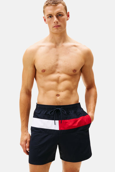 Short de bain bleu Tommy Jeans avec une rayure rouge et blanche, porté par un mannequin.