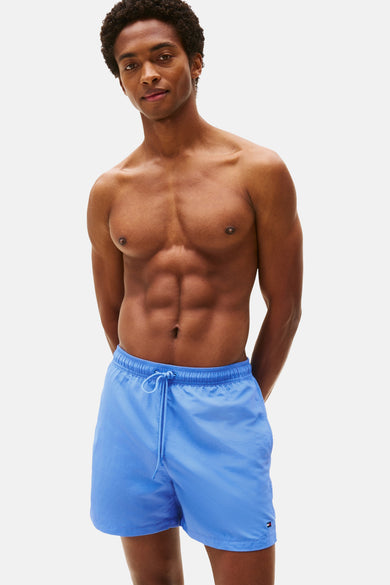 Short de bain bleu Tommy Hilfiger, avec cordon de serrage et logo sur la jambe, porté par un mannequin torse nu.