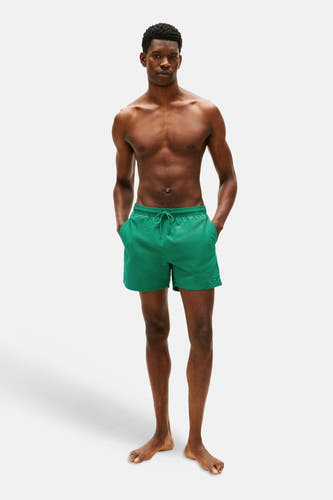 Groene zwemshort van Tommy Hilfiger, gedragen door een man met zijn handen in de zakken.