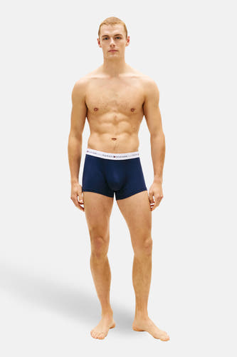 Boxer short bleu foncé de Tommy Jeans, porté par un homme au torse musclé, debout sur un fond blanc.