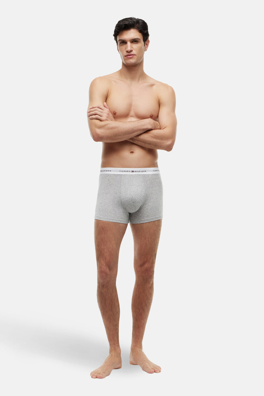 Boxer short gris de TOMMY JEANS, porté par un homme les bras croisés et pieds nus.