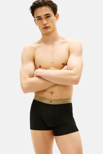 Boxer short noir de TOMMY JEANS, présenté avec une ceinture élastique à logo de la marque, porté par un mannequin les bras croisés.