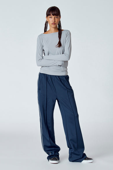 T-shirt gris à manches longues d'Unwind, avec des manches longues et un modèle aux cheveux tressés, un pantalon bleu et des chaussures.
