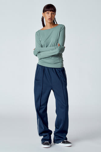 T-shirt vert avec manches longues d'Unwind, porté avec un pantalon bleu marine et des baskets.