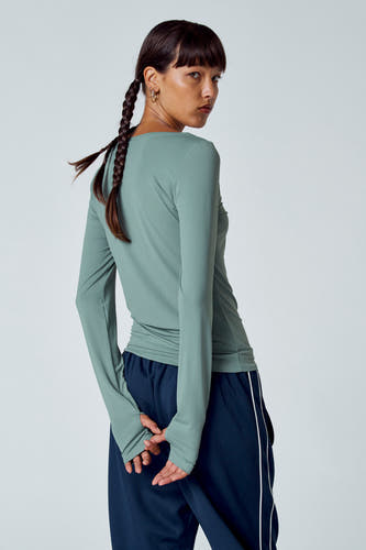 Groen T-shirt met lange mouwen van Unwind, met duimgaten en een sportieve broek met witte strepen.
