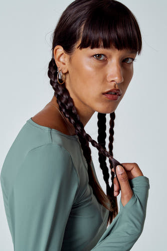 T-shirt vert avec manches longues d'Unwind, avec deux tresses et des boucles d'oreilles dorées.