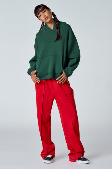 Pull-over vert de Unwind avec capuche, avec une poche et porté avec un pantalon rouge et des baskets.