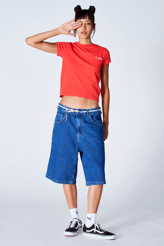 T-shirt rouge à manches courtes d'Unwind, porté avec des jeansshorts larges et des chaussures noires avec des chaussettes blanches.