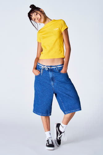 T-shirt jaune à manches courtes d'Unwind, porté avec des shorts de denim amples et des baskets noires et blanches.