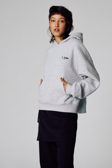 Pull-over gris avec capuche d'Unwind, avec des poches à l'avant et porté avec une jupe noire.