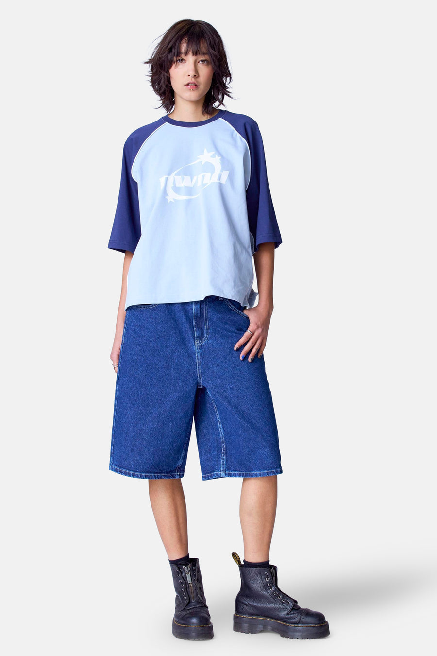 Jonge vrouw in blauw shirt, denim shorts en zwarte laarzen.