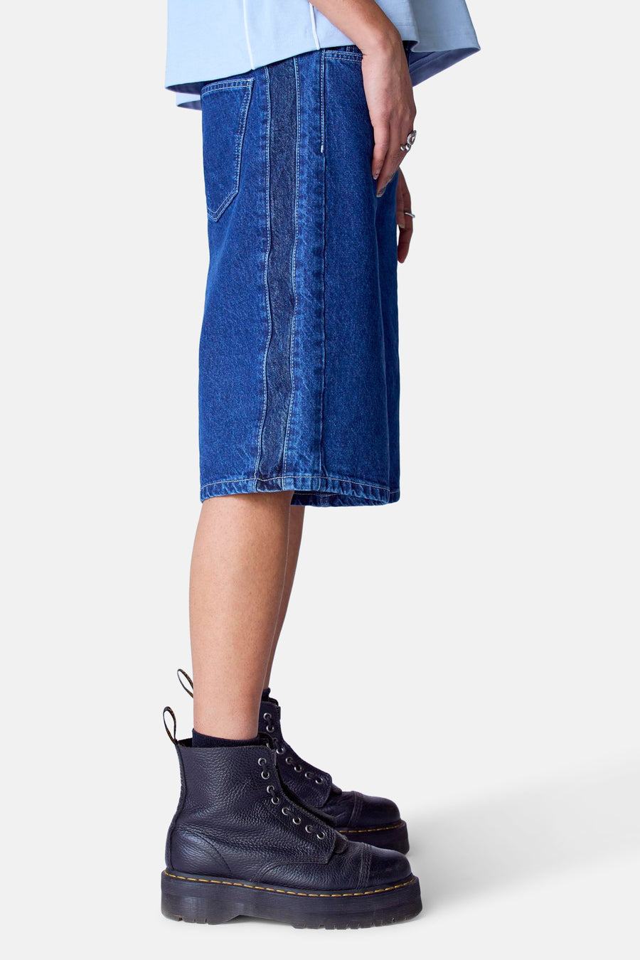 Persoon met een blauw shirt en een blauwe denim rok, draagt zwarte leren veterlaarzen met dikke zolen.