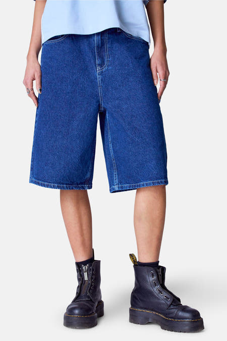 Short en denim bleu marine d'Unwind, porté avec des bottes noires à fermeture éclair et un t-shirt bleu clair.