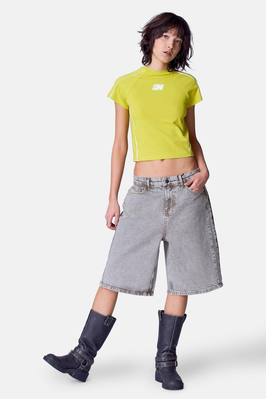 Jonge vrouw, geel shirt, grijze bermuda, zwarte laarzen.