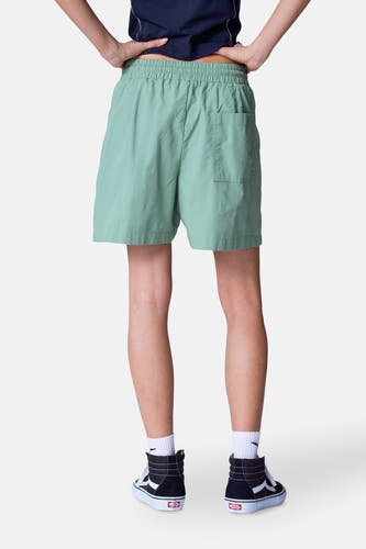 Short vert de Unwind, vu de l'rière, avec une ce taille élastique et un poche arrière, associé à des chaussettes blanches et des baskets Vans noires.