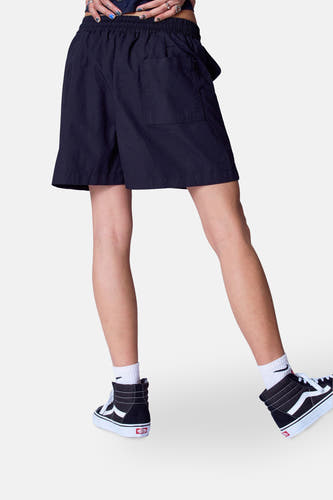 Short noir d'Unwind avec poches, porté avec des baskets Vans hautes et des chaussettes blanches.