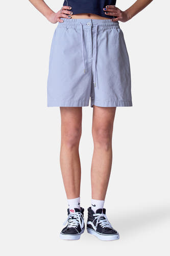 Short gris d'Unwind, avec une ceinture élastique et des poches, porté avec des sneakers hautes et des chaussettes blanches.
