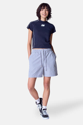 Short gris d'Unwind, avec une ceord et portéé un top bleu foncé et des baskets hautes.