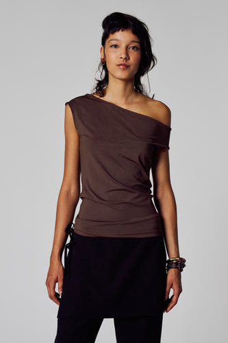 T-shirt marron à manches courtes d'Unwind, avec une ligne de col asymétrique, porté avec une jupe noire et des bracelets colorés.