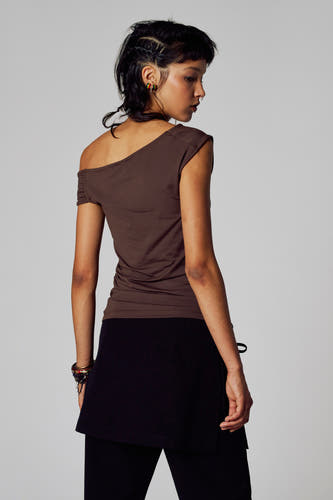 T-shirt marron à manches courtes d'Unwind, avec un seul épaule dénudée, associé à une jupe noire et une pantalon.