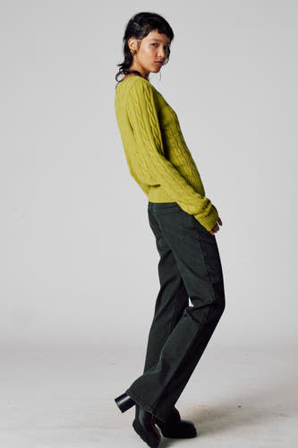 T-shirt V-hals vert de Unwindwind avec un motif motif tr et et et longues manches, associé à des pantalons foncés et des bottes noires.