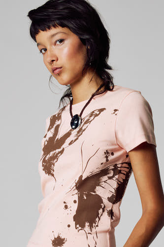 T-shirt rose à manches courtes d'Unwind, avec imprimé de papillon marron et le modèle porte une chaîne argentée.