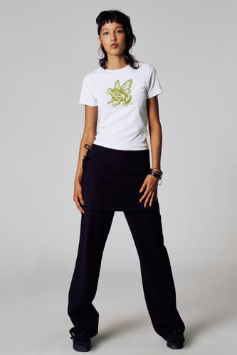 T-shirt blanc à manches courtes d'Unwind, avec imprimé de grenouille verte et porté avec un pantalon noir.
