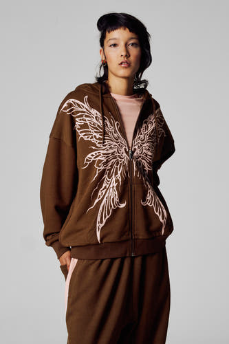 Veste brune Unwind, vue de derrière, avec capuche et longues manches, portée avec un pantalon coordonné.